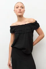 Blusa negra estilo bardot con escote de hombros descubiertos, detalles de volados fruncidos en el pecho y diseño sin mangas.