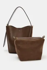 Bolso tipo saca con diseño estructurado, confeccionado en una combinación de cuero liso y gamuza en tono marrón. Cuenta con asa de hombro fija, cierre imantado y detalles metálicos en dorado.