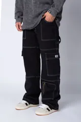 Pantalón tipo carpintero de corte relaxed fit y tiro medio, confeccionado en denim negro con costuras a contracolor en blanco. Presenta múltiples bolsillos cargo laterales, un bolsillo con cierre en la parte inferior y presillas utilitarias.