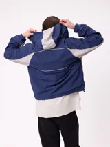 Rompevientos Rusty con capucha, diseño bicolor en azul marino y gris, cierre frontal y logo bordado en el pecho.