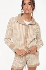 Cardigan de punto con patrón trenzado, color crudo y visón, con cuello solapa, cierre frontal de botones y mangas largas con puños elásticos rayados.