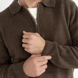 Buzo de tejido de punto color marrón, con cuello polo y cierre frontal parcial, de manga larga con puños y ruedo acanalados.
