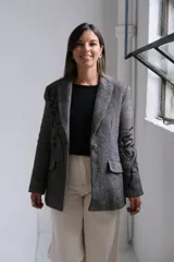 Blazer de corte sastrero en color gris con patrón de rayas diagonales y bordados negros en las mangas y solapas. Presenta cierre frontal con botón, bolsillos con solapa y estructura clásica.