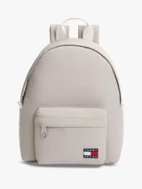 Mochila Tommy Jeans de color beige, diseño compacto y curvo, con compartimento principal con cierre de cremallera, bolsillo frontal con cremallera y parche con el logo de la marca. Cuenta con asas ajustables y acolchadas.