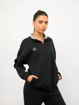 Buzo de felpa negro con medio cierre frontal, cuello alto con interior en color gris y logo de la marca bordado en el pecho. Presenta bolsillos laterales y puños elásticos.