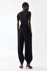Pantalón de sarga negro de tiro alto con bolsillos laterales discretos y cierre con botón y corchetes ocultos. Presenta diseño de piernas globo con pinzas y puños abotonados con frunces.