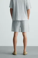 Bermuda negra de corte regular, confeccionada en tejido jacquard con efecto arrugado. Presenta cintura elástica ajustable con cordón blanco, bolsillos laterales y bolsillos traseros de vivo.