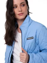 Chaqueta acolchada de color azul claro con diseño de costuras en zigzag. Presenta cierre frontal, cuello alto, bolsillos laterales con cierre y parche con logo de la marca en el pecho.