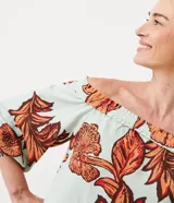 Blusa celeste con estampado de hojas color naranja y marrón, con escote hombro a hombro, mangas 3/4 con lazos en los puños y corte holgado.