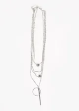 Collar plateado de cuatro cadenas finas de diferentes largos, con dijes colgantes: dos dijes circulares con incrustaciones y un dije de barra vertical unida a un aro.