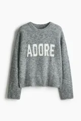 Buzo de punto gris melange con diseño jacquard y la palabra 'ADORE' en blanco en el frente, cuello redondo y hombros caídos.