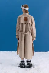 Trench midi de color camel, confeccionado en una mezcla de algodón y nylon con propiedades repelentes al agua. Presenta un diseño clásico con cuello camisero, cierre frontal de botones, bolsillos laterales y tajos en los costados.