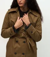 Trench coat largo de Marfinno, confeccionado en gabardina de poliéster. Presenta cuello con solapas, aletas en los hombros, cierre frontal con botones y cinta para lazo en la cintura.