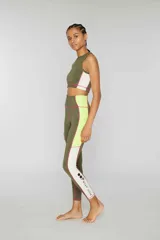 Crop top deportivo verde oliva sin mangas de lycra con banda lateral color block en amarillo y rosa y pespuntes overlock en contraste. Estampado de logotipo en la parte delantera.