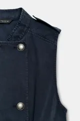 Top estilo chaleco de color azul marino, con cuello mao, sin mangas y trabillas en los hombros. Cuenta con cierre frontal cruzado mediante botones metálicos y bolsillos delanteros de plastrón con solapa.