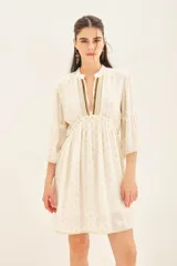 Vestido corto blanco con estampado de puntos dorados, mangas al codo con volados y ajuste en la cintura. Escote en V con detalles bordados en dorado y negro.