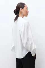 Camisa blanca de manga larga con puños abotonados y fruncidos, hombros fruncidos y cierre frontal con botones.
