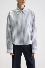 Camisa de calce relajado confeccionada en algodón, con diseño de rayas verticales celestes y blancas. Presenta cuello clásico, cierre frontal con botones y puños anchos abotonados.