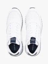 Zapatillas deportivas Tommy Hilfiger de corte bajo, inspiradas en modelos clásicos de running. Presentan un exterior en mezcla de piel blanca con paneles de texturas mixtas, detalles de ventilación en la parte superior y suela de goma con tacos. Incluyen cordones y logo de la marca en el lateral, lengüeta y parte trasera.