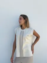 Top sin mangas tejido en hilo color crema, con cuello redondo y rayas verticales grises. Presenta un logo bordado en el pecho.