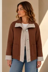 Campera marrón de lino con diseño bicolor, con una franja central gris claro que incluye botones de nácar. Cuenta con cuello alto, mangas largas con puños grises, bolsillos frontales aplicados y silueta amplia.