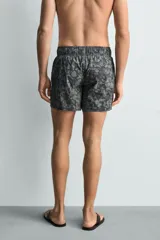 Bañador de hombre de tejido técnico, color gris oscuro con estampado abstracto en tonos más claros. Presenta cintura elástica ajustable con cordón, bolsillos laterales y un bolsillo trasero de plastrón.