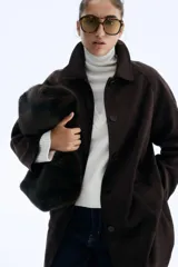 Abrigo largo hasta la rodilla, color marrón oscuro, con acabado cepillado suave. Presenta cuello camisero, manga raglán, botonadura frontal y bolsillos laterales insertados. Tiene forro interior y abertura en la espalda.