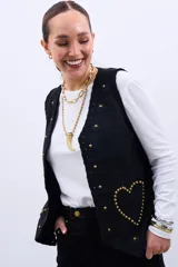 Chaleco negro con apliques de flores y tachas doradas en forma de corazón.