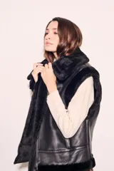 Chaleco negro de cuero sintético con cuello de piel sintética y cierre frontal con cremallera.