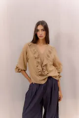 Camisa de algodón color tostado con escote en V y volados frontales con detalles de encaje. Mangas tres cuartos abullonadas con puños elásticos fruncidos.