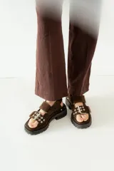 Sandalias de plataforma estilo chunky color marrón, confeccionadas en gamuza. Presentan tiras ajustables con hebillas metálicas y detalles de ojales plateados, con suela de goma dentada.