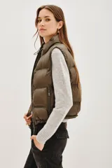 Chaleco acolchado de corte corto, color verde oliva, con cuello alto ajustable mediante cordones elásticos y cierre frontal con cremallera.