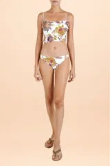 Top de bikini con escote recto y breteles finos, presenta un diseño con volado asimétrico en la base y estampado botánico multicolor sobre fondo blanco.