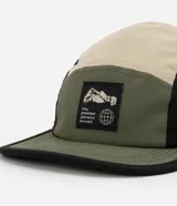 Gorra tipo 5 panel confeccionada en microfibra de poliamida, con diseño de bloques de colores en beige, negro y verde oliva. Presenta visera recta, cierre posterior ajustable y etiqueta frontal con gráfico y frase Stay Grounded.