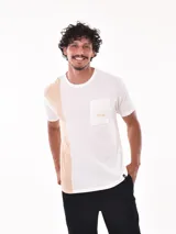Remera de manga corta con diseño bicolor, combinando blanco y beige. Presenta un bolsillo frontal en el lado izquierdo con el logo de la marca estampado en color naranja.