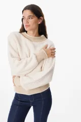 Sweater de punto grueso con diseño bicolor, cuerpo en color crema y detalles en color beige en cuello, puños y ruedo. Presenta mangas largas con caída relajada y cuello redondo.