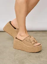 Sandalias de plataforma alta con diseño tipo zueco, color tostado, elaboradas en gamuza. Poseen capellada abierta con detalles de costuras perforadas y borlas colgantes decorativas.