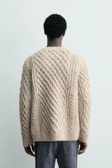 Jersey de punto con diseño de trenzas diagonales, confeccionado en lana con efecto moteado. Presenta cuello redondo, manga larga y terminaciones en rib.