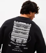 Buzo de algodón negro con felpa interna, corte boxy, cuello redondo y manga larga. Presenta un gran estampado en la espalda con la ilustración de un hotel clásico y texto en color blanco.