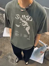 Remera marrón oversize con efecto acid wash, corte amplio y mangas cortas. Presenta un estampado frontal en tonos celestes y grises con la inscripción 'Sumo', una ilustración de un luchador de sumo y detalles tipográficos alusivos a un álbum musical.