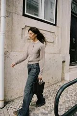 Chaqueta de punto color beige, de manga larga y corte corto, con cuello redondo y puños terminados en puntilla blanca a contraste.