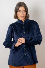 Camisa de pana azul marino con cuello alto tipo mao con volados, cierre frontal de botones y mangas largas con puños abotonados.