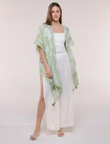 Kimono de gasa verde con estampado de hojas blancas y detalles de lurex. Presenta mangas cortas holgadas, diseño abierto al frente y terminación en punta con borlas en el ruedo.