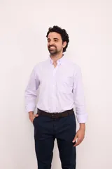 Camisa de corte clásico confeccionada en algodón, con diseño de rayas verticales finas en color rosa sobre fondo blanco. Presenta cuello abotonado, cierre frontal con botones, mangas largas con puños abotonados y un bolsillo en el pecho con el logo de la marca bordado.