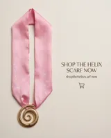 Pañuelo de seda con diseño estampado en tonos rosados y rojos, combinado con un dije dorado en forma de espiral.