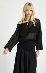 Blusa negra de punto calado con diseño amplio y transparente, escote de hombros descubiertos, mangas largas y puños acampanados.