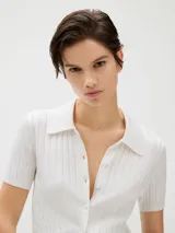 Top corto de punto acanalado color blanco, con cuello tipo chomba y cierre frontal abotonado.