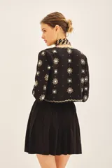 Saco corto de corte entallado con escote redondo, confeccionado en tejido negro con bordados artesanales de lentejuelas y pedrería en forma de estrellas y motivos florales en frente, espalda y mangas.
