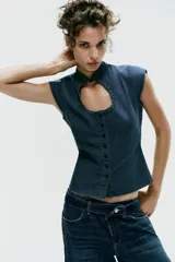 Top entallado de efecto denim, con cuello subido, manga corta, cierre frontal con botones y una llamativa abertura circular en el pecho.