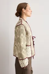 Chaqueta capitoneada de diseño acolchado con estampado paisley en tonos beige y verde, con ribetes y lazos de cierre frontales en color bordó.